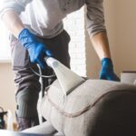 Dry cleaner's man employee removing dirt from furniture in flat, closeup, vacuum clean sofa with professional equipment