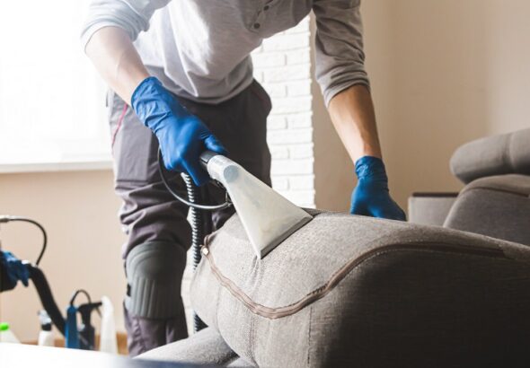 Dry cleaner's man employee removing dirt from furniture in flat, closeup, vacuum clean sofa with professional equipment